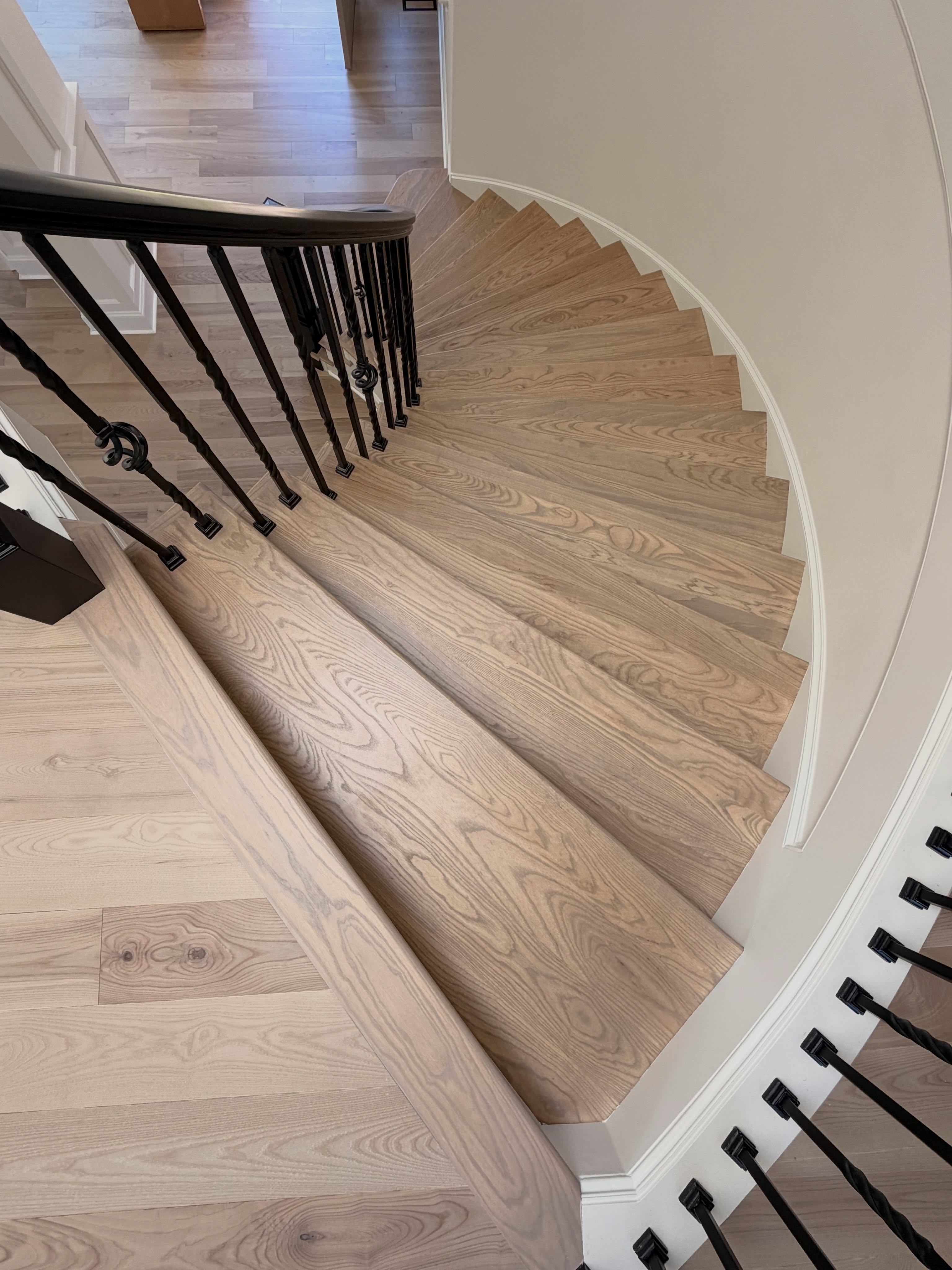 Curved staircase finished in wide plank oak with wrought iron balusters